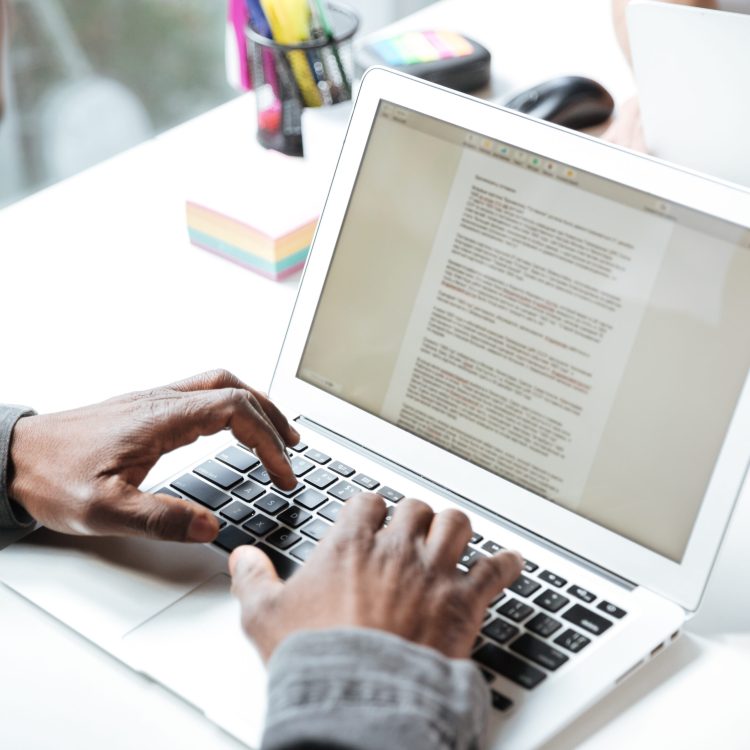 Cropped photo of serious young man sitting in office coworking. Looking aside using laptop computer. Focus on computer.